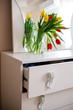 Sarı ve kırmızı lale buketi cam vazoda, beyaz şifoniyer üzerinde ayna, rahat ev içi