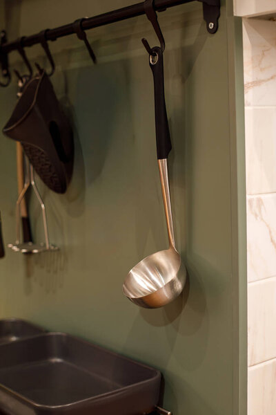 Metal soup ladle hanging on kitchen rail in modern minimalist kitchen interior