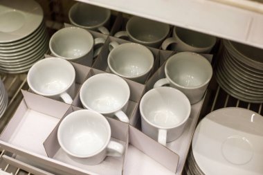 Beyaz seramik bardaklar, tabaklar ve tabaklar ile dolu kutular içinde, perakende iç kısımda sergilenen minimalist kahve tabakları, sığ alan derinliği olan temiz modern mutfak gereçleri konsepti