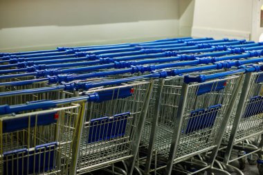 Bir süpermarketin içine düzgünce istiflenmiş mavi saplı boş alışveriş arabaları, temiz perakende iç mekan düzeni, hazırlık, tüketici hizmeti ve modern alışveriş kolaylığı