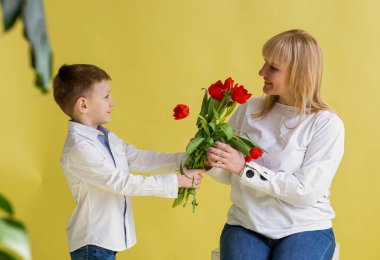 Genç bir çocuk annesine bir buket kırmızı lale veriyor. Stüdyo ortamında sevgi ve minnettarlık anı.