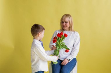 Genç bir çocuk annesine bir buket kırmızı lale veriyor. Stüdyo ortamında sevgi ve minnettarlık anı.