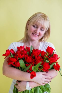 Büyük bir buket kırmızı lale tutan gülümseyen bir kadının portresi, mutluluk, sevgi ve kutlamayı ifade eder, Anneler Günü, Sevgililer Günü ve parlak bir stüdyo ortamında doğum günü kutlamaları ile ilişkilendirilir..