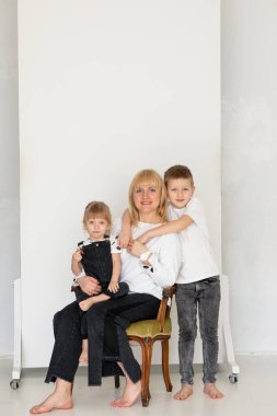 Mutlu anne, oğlunu ve kızını parlak bir stüdyoda kucaklıyor, sevgi, ilgi ve samimiyet gösteriyor, anneliği, aile bağlarını ve Anneler Günü ve Uluslararası Kadınlar gibi kutlama anlarını sembolize ediyor.