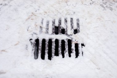 Metal rögar ızgarası kış caddesinde kısmen karla kaplı. Soğuk havada kentsel drenaj sistemi