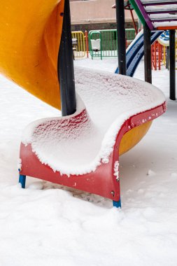 Kış günü yumuşak karla kaplı oyun alanı kaydırağını kapat. Soğuk şehir bahçesinde donmuş parlak plastik yüzey
