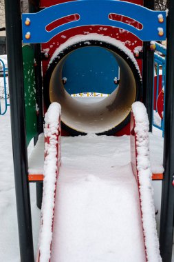 Oyun alanı tüneli girişinin önü kışın karla dolu. Kar yağışı sırasında konut avlusunda renkli yapı boş duruyor