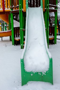 Yeşil plastik kaydırak, kış parkındaki boş çocukların oyun parkında taze beyaz karla kaplı.