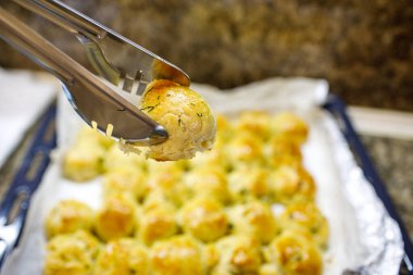 Altın sarımsaklı otlar, yemek tepsisinden metal maşalar, kabarık tereyağı kabuğu ve yumuşacık iç döşeme, ev yapımı ekmek.