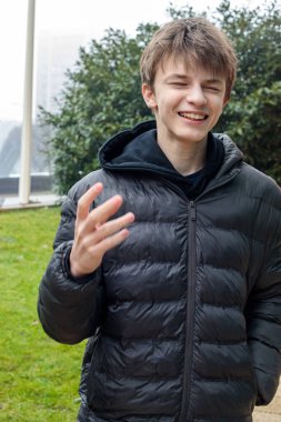Gülümseyen genç çocuk parkta gülüyor. Siyah kapüşonlu ve kabarık ceketli, modern gençlik yaşam tarzının samimi duygusal portresi.