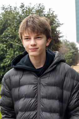 Parkta duran ceketli bir gencin açık hava portresi, sakin gençlik ifadesi ve otantik modern yaşam tarzı atmosferi