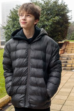 Parkta duran ceketli bir gencin açık hava portresi, sakin gençlik ifadesi ve otantik modern yaşam tarzı atmosferi