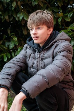 Siyah kapüşonlu ve kabarık ceketli gülümseyen bir gencin açık hava portresi, neşeli bir ifade ve otantik modern sokak gençlik yaşam tarzı.