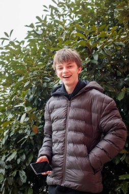 Siyah kapüşonlu ve kabarık ceketli gülümseyen bir gencin açık hava portresi, neşeli bir ifade ve otantik modern sokak gençlik yaşam tarzı.