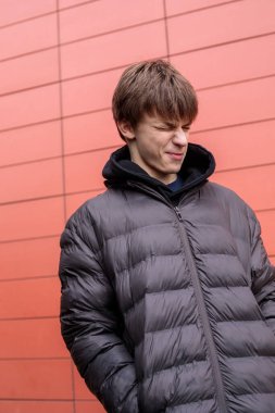 Siyah kabarık ceketli oyuncu çocuk kırmızı duvara bakarken komik surat yapıyor. Kopya alanı olan kentsel yaşam tarzı portresi.