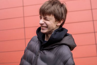 Siyah kabarık ceketli oyuncu çocuk kırmızı duvara bakarken komik surat yapıyor. Kopya alanı olan kentsel yaşam tarzı portresi.