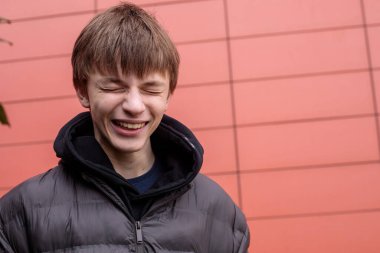 Siyah kabarık ceketli oyuncu çocuk kırmızı duvara bakarken komik surat yapıyor. Kopya alanı olan kentsel yaşam tarzı portresi.