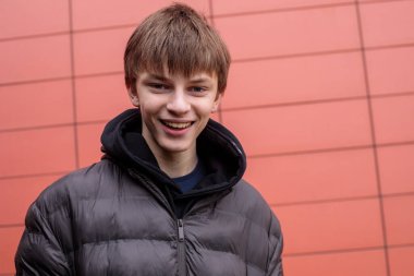 Siyah kabarık ceketli, gülümseyen bir gencin, modern kırmızı duvara bakan, doğal şehir yaşam tarzı konsepti.