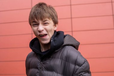 Siyah kabarık ceketli oyuncu çocuk kırmızı duvara bakarken komik surat yapıyor. Kopya alanı olan kentsel yaşam tarzı portresi.