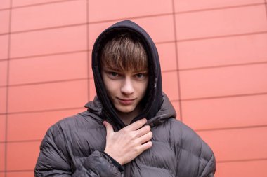 Kapüşonlu ceketli, modern kırmızı duvara bakarken kameraya bakan, fotokopi çekilen yoğun şehir portresi.