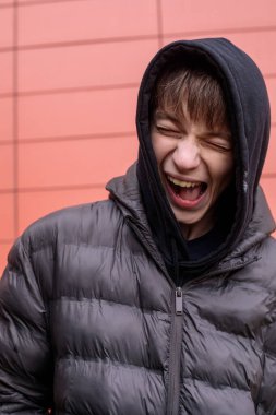 Siyah kabarık ceketli oyuncu çocuk kırmızı duvara bakarken komik surat yapıyor. Kopya alanı olan kentsel yaşam tarzı portresi.