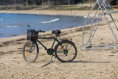 Bisiklet, sakin denizin yanında kumlu sahilde duruyor ve nazik dalgalar. Sahil şeridi ve mavi suyu olan güneşli sahil manzarası, aktif yaşam tarzı ve seyahat kavramı