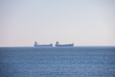 Bulgaristan 'ın Varna kenti yakınlarındaki Karadeniz' in ufuklarında yük gemileri görülüyor. Sakin su, hafif sis ve kıyı açıklarında bekleyen büyük taşıyıcılarla endüstriyel deniz atmosferi.