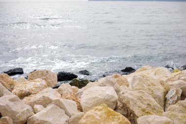 Yumuşak dalgalar ve dokulu kıyı taşlarıyla kayalık sahil kıyısı, minimum doğal deniz manzarası arka planı