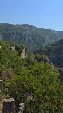 Bulgaristan 'da, açık mavi gökyüzü altında yemyeşil ağaçlarla çevrili ormanlık tepeler ve kayalık yamaçlar manzaralı bir yaz manzarası yaratıyor.