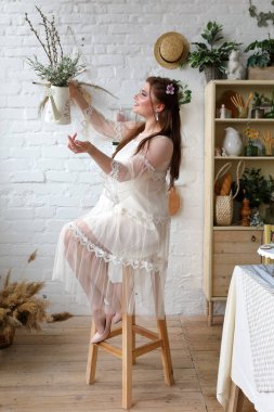 Kırsal evin iç kısımlarında bahar buketi olan zarif genç bir kadın, mevsimlik dekorlu neşeli paskalya tarzı bir portre.