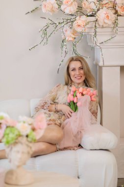 Bir buket pembe laleyle gülümseyen kadın çiçek açan dalların altında dinleniyor, baharı kutluyor, kadınlar gününü kutluyor ve zarif iç mekanlarda anneler gününü kutluyor.