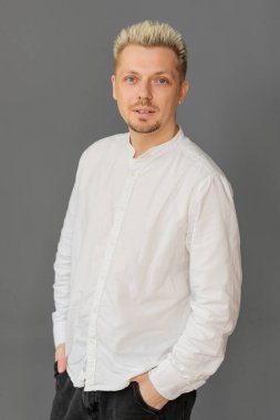 Kendine güveni tam genç bir adam elleri ceplerinde tarafsız gri arka planda, rahat duruş, sakin ifade ve çağdaş yaşam tarzını gösteren modern bir portre.