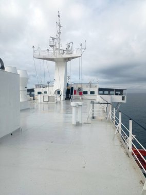 Köprü ve dümenli gemi güvertesi bulutlu gökyüzünün altında, ıslak yüzeyi ve açık deniz ufkuyla deniz taşımacılığı sahnesi