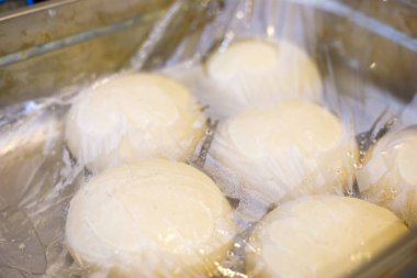 Çiğ hamur topları metal tepsiye sarılı, fırın mutfağında hazırlık aşaması.