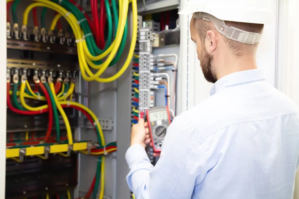 Electrician engineer measures voltage in power electrical cabinet. Serviceman adjusts fuse box.