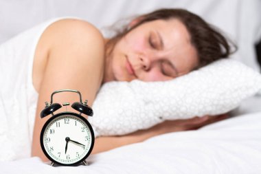 Genç bir kadın yatakta uyuyor ve çalar saatin çalmasını bekliyor. Bir kadın yatakta uyanır.