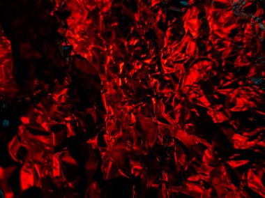 Crumpled aluminum foil with a striking red hue, creating a textured, abstract appearance. 