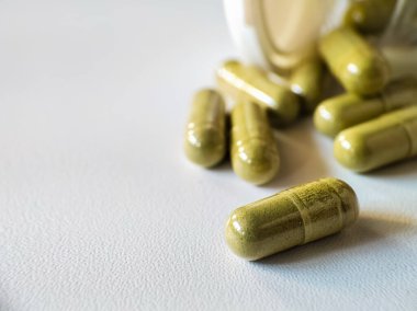 Close up of green capsules scattered across a smooth, white surface. 