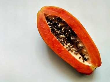 Canlı turuncu eti ve sayısız siyah tohumu sergilenen olgun papaya pürüzsüz beyaz bir yüzeye yerleştirilir.. 