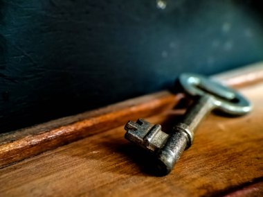 Eski, metal bir anahtar, arkasında koyu bir arka plan bulunan ahşap bir yüzeyde duruyor.. 