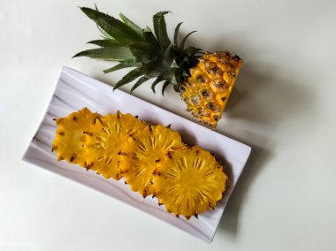 Dilimlenmiş bir ananas beyaz, tırtıklı bir tabakta sergilenir..