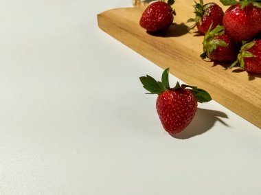 Taze çilekler pürüzsüz beyaz bir yüzeyde dinleniyor. Farklı gölgeler bırakıyor..