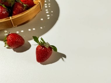 Taze çilekler pürüzsüz beyaz bir yüzeyde dinleniyor. Farklı gölgeler bırakıyor..