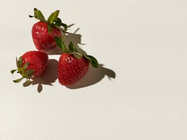 Taze çilekler pürüzsüz beyaz bir yüzeyde dinleniyor. Farklı gölgeler bırakıyor..