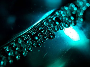 Teal renkli ışık, kabarcıkların yakın plan çekimini aydınlatır ve yüzey boyunca bir çizgi oluşturur.. 