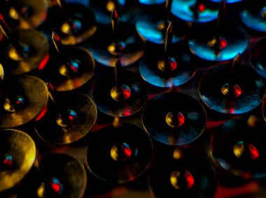 Parlak kırmızı, mavi ve altın ışıklı, birbirine yakın dizilmiş metalik başparmak raptiyeleri kümesi. 