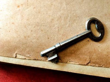 Eski bir metal anahtar desenli, bej bir kağıt yüzeyde duruyor..