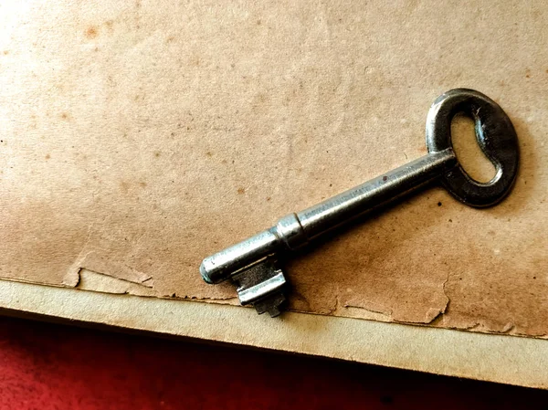 Eski bir metal anahtar desenli, bej bir kağıt yüzeyde duruyor..