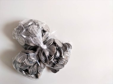 Temiz beyaz bir yüzey üzerinde duran gümüş para yığınlarıyla dolu temiz plastik torbalar. Bu düzenleme tasarruf, mali yönetim veya para birikimi temalarını önerir.
