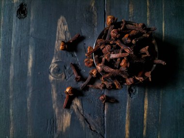 Kurumuş karanfillerle dolu küçük bir kase, koyu ahşap bir yüzeye oturur..